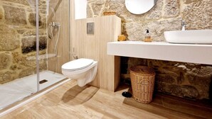 Une salle de bain avec un mur en pierre, une douche en verre, des toilettes, un lavabo et un panier en osier.