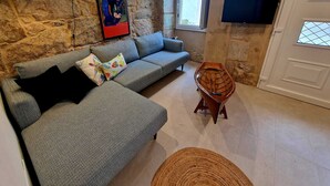 Un salon avec un canapé gris, des coussins colorés, un bateau en bois, une lampe, un tableau et un téléviseur accroché au mur.