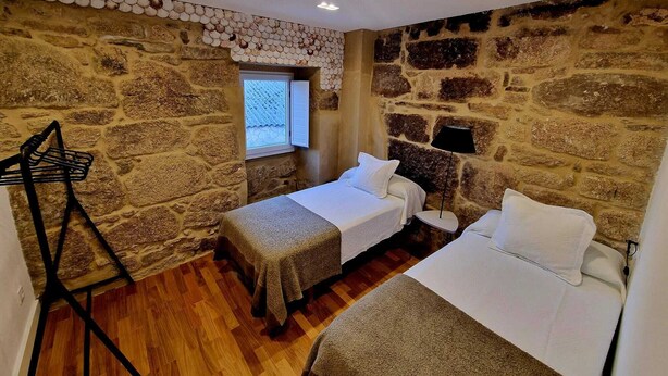 Une chambre avec deux lits, une fenêtre et des murs en pierre.