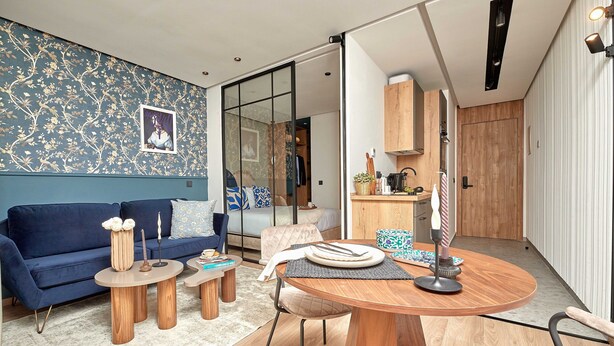 A modern living room with a blue sofa, wooden coffee table, and a dining area with a wooden table and chairs.
