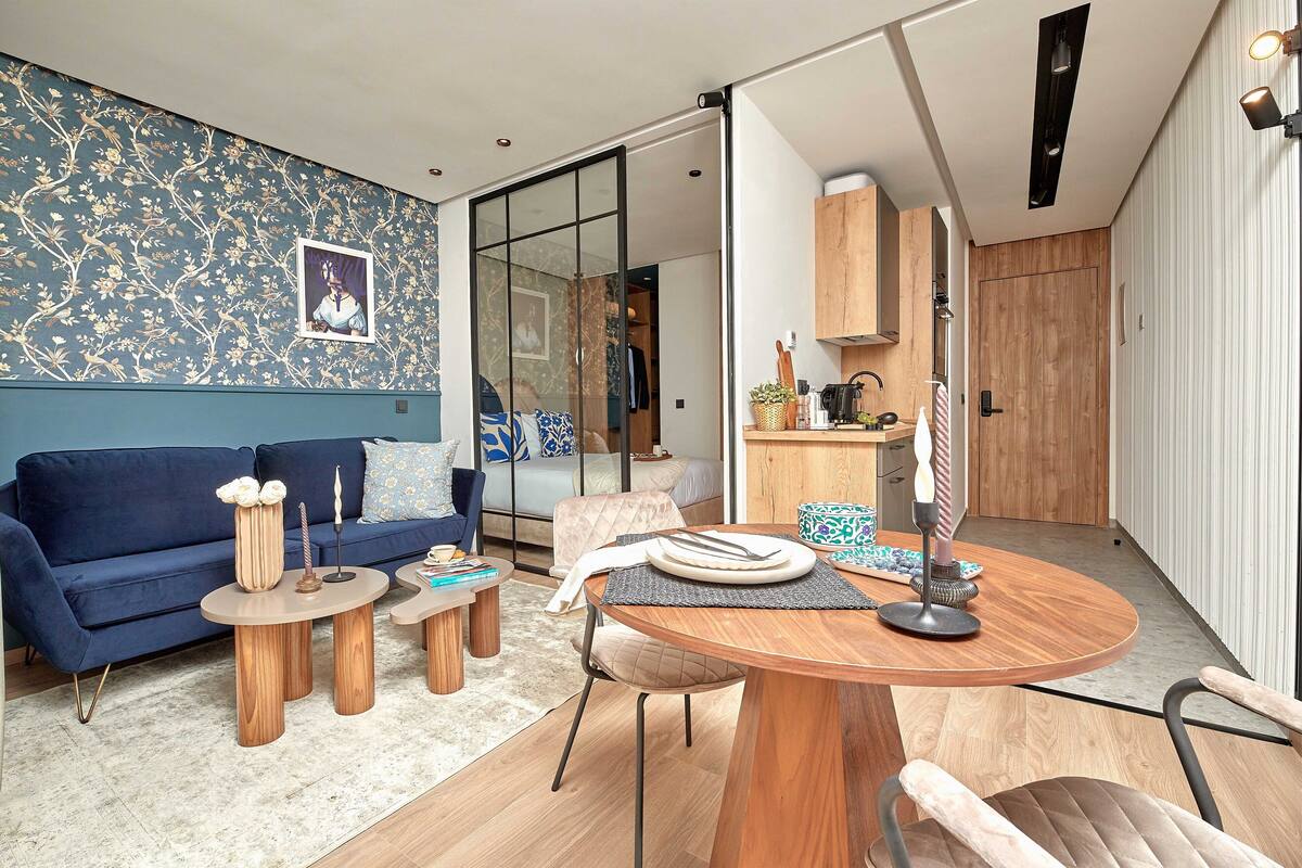 A modern living room with a blue sofa, wooden coffee table, and a dining area with a wooden table and chairs.
