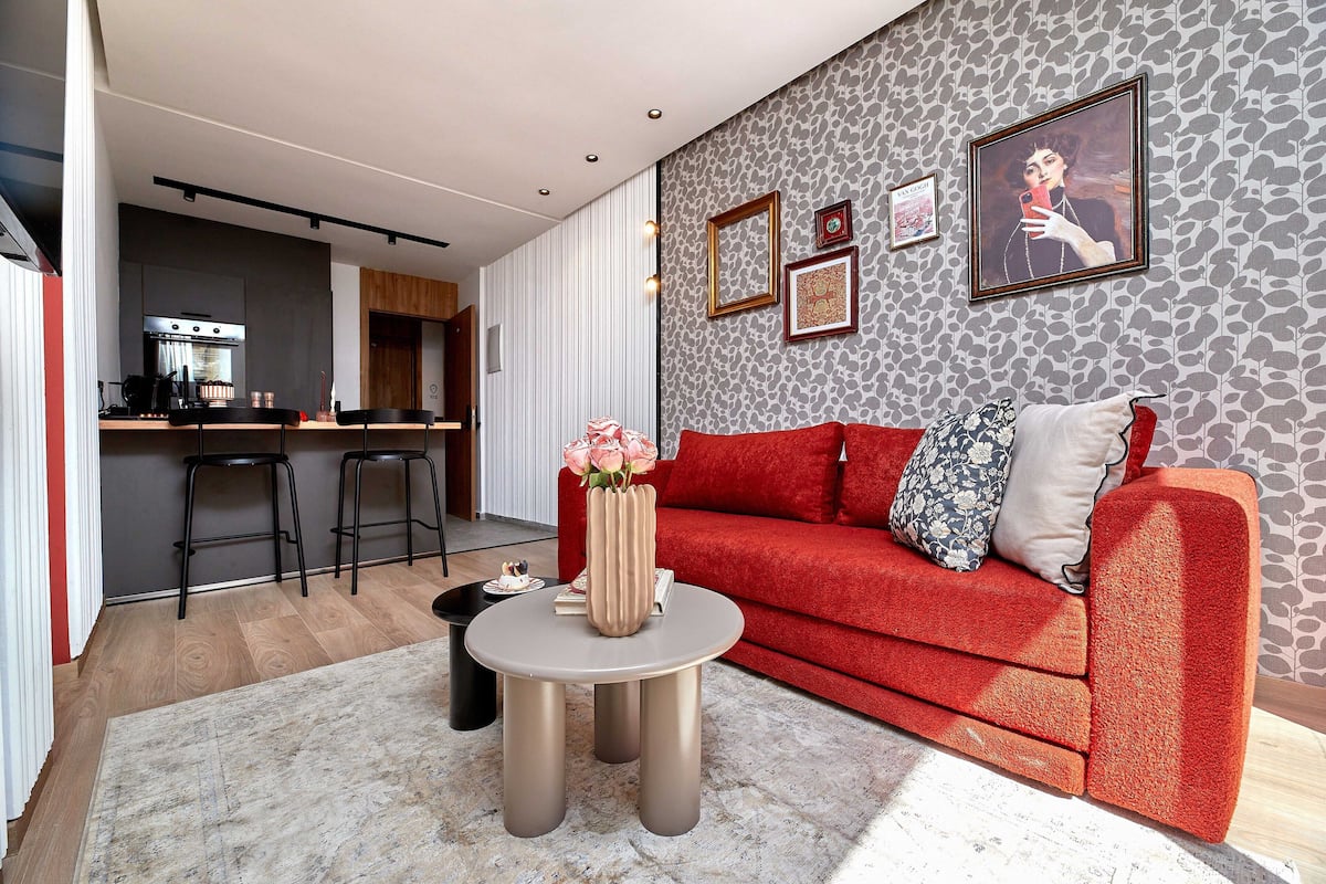 A modern living room with a red sofa, a round coffee table, and a kitchen in the background.
