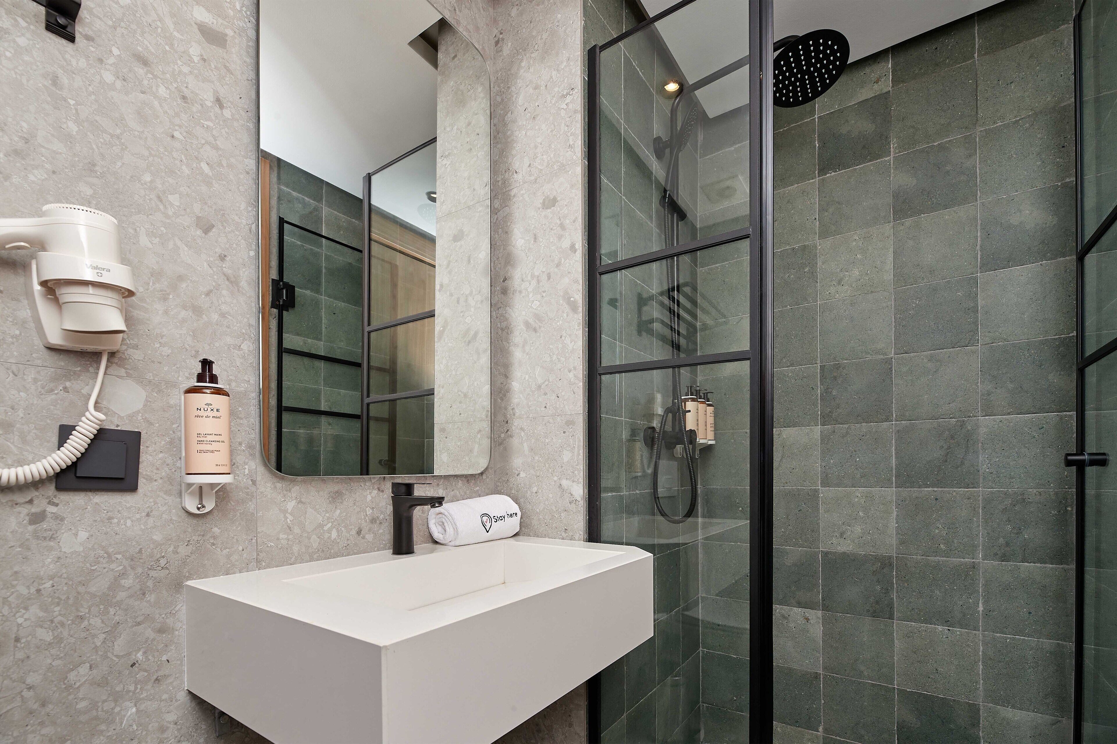 A modern bathroom with a white sink, a hairdryer, and a shower with a glass door.