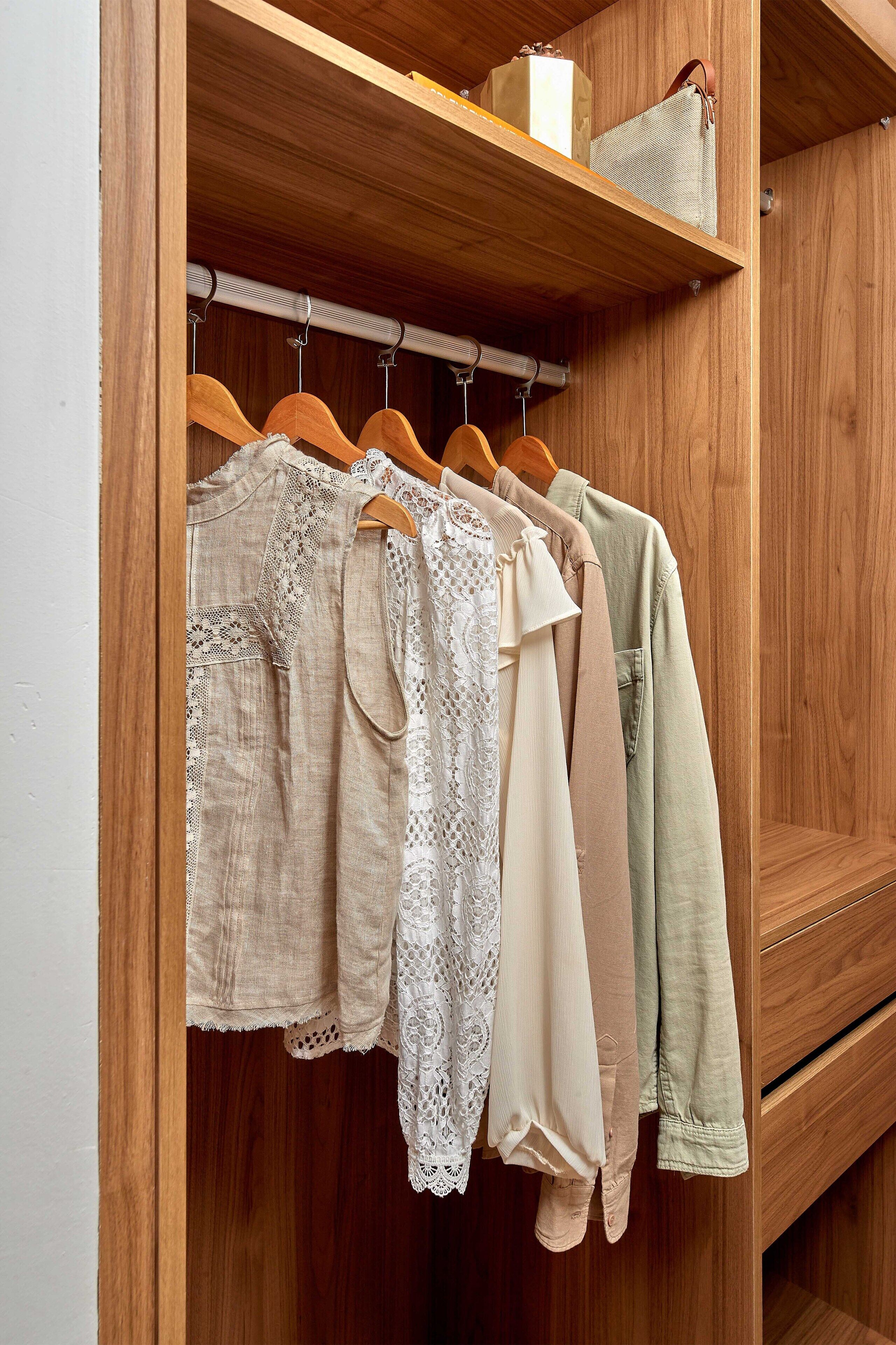 A wooden closet with hanging clothes and a shelf with a bag.
