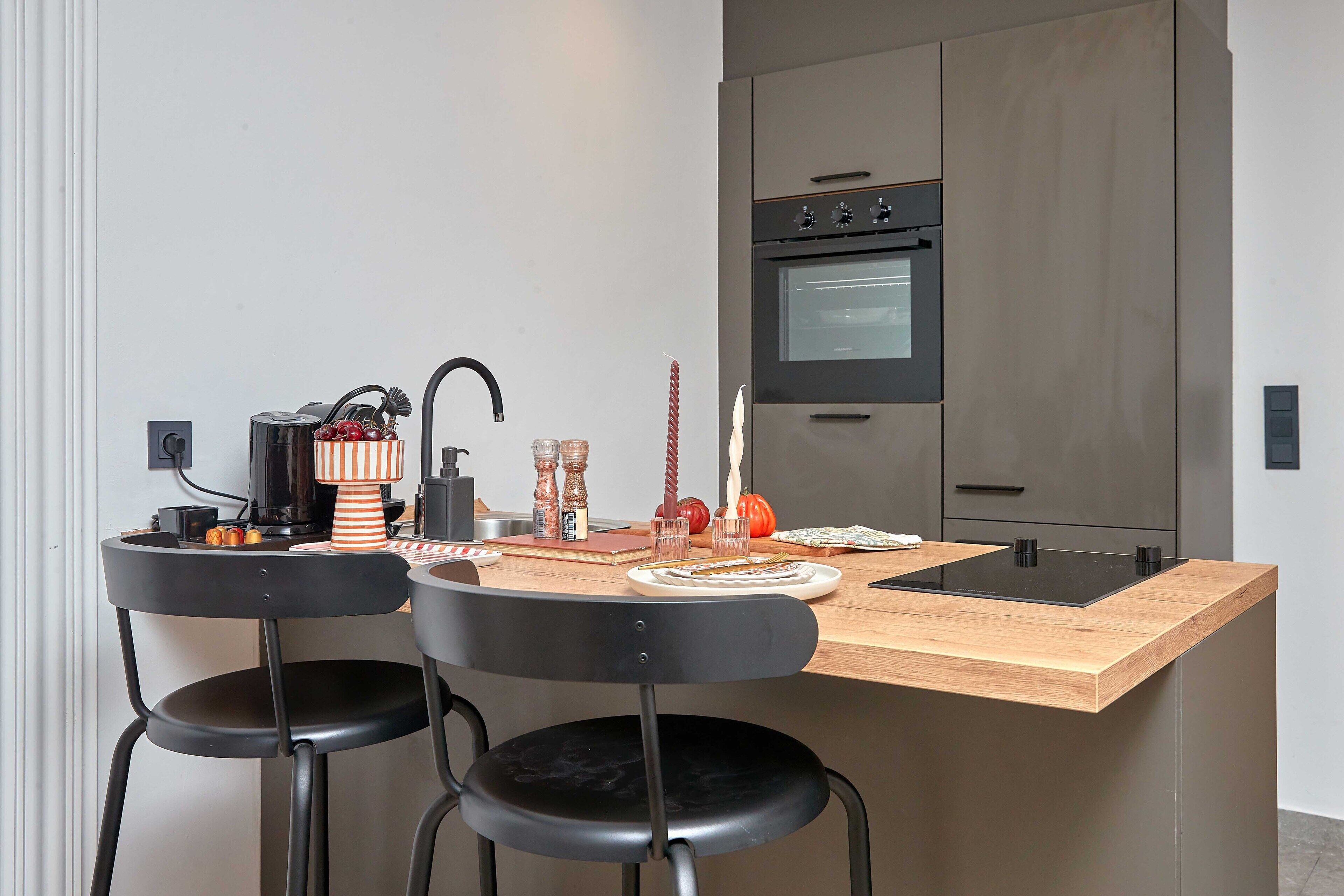 Une cuisine moderne avec un îlot central en bois, deux chaises noires et un four encastré.