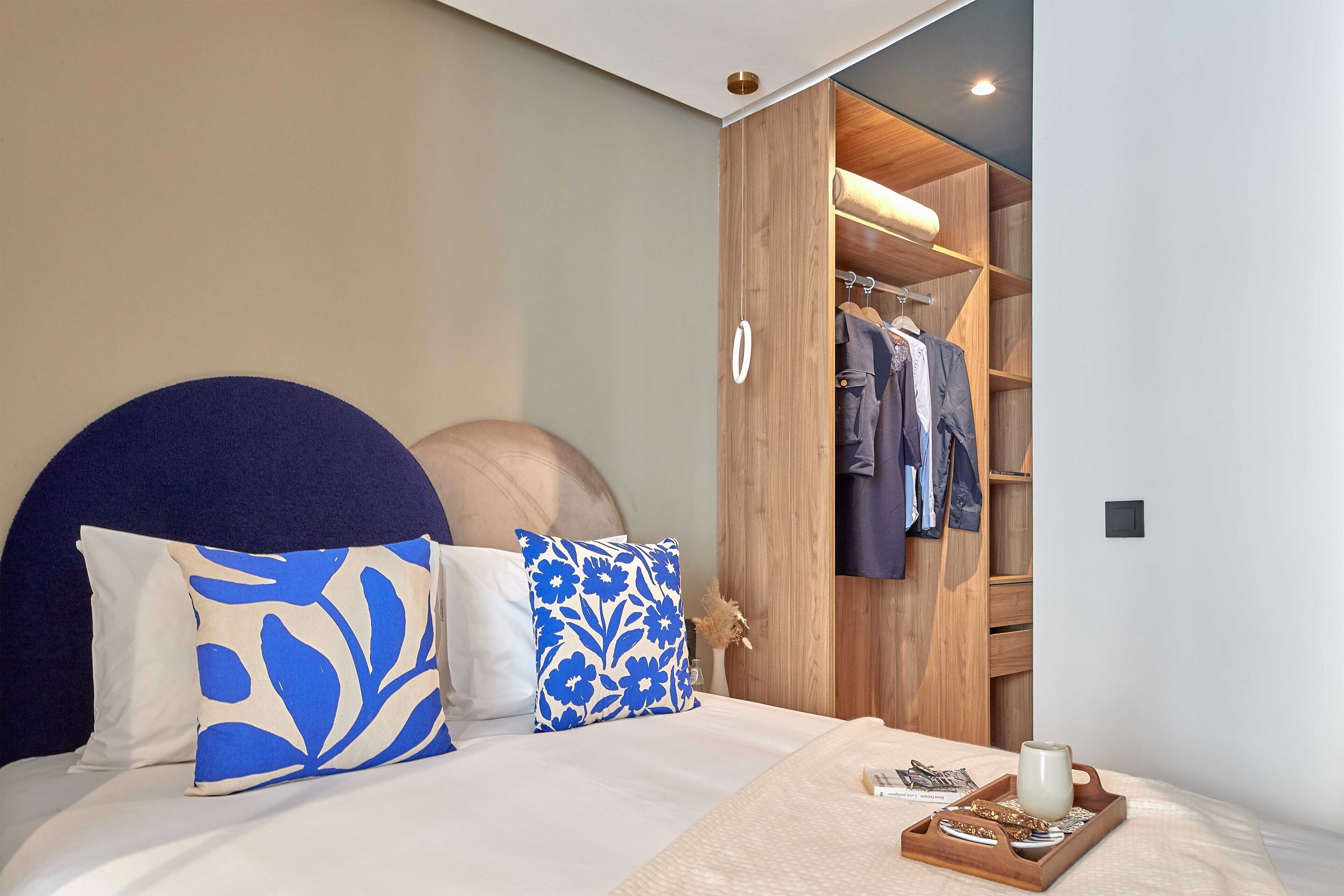 Un dormitorio con cama, armario de madera y mesita de noche con taza y aperitivos.