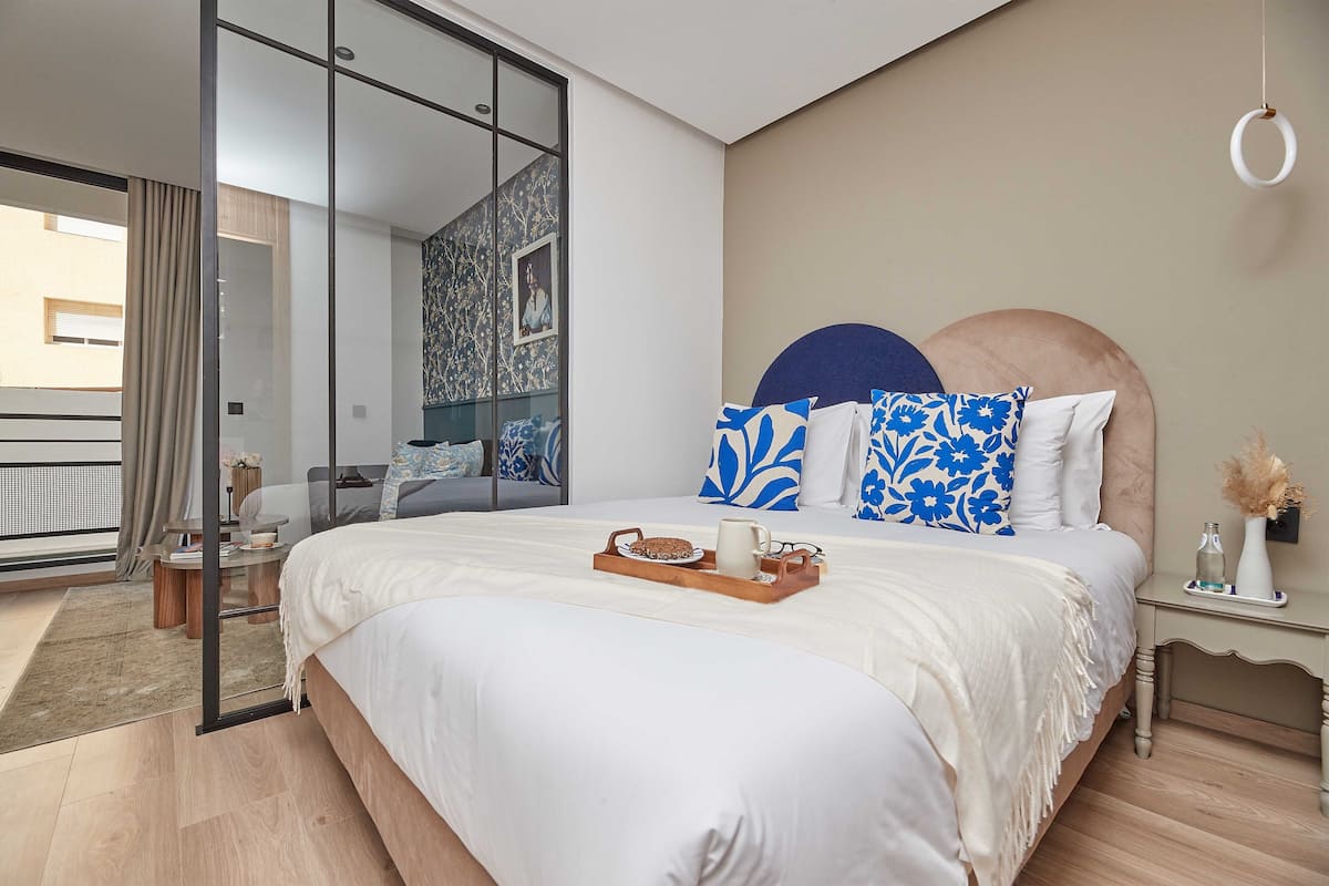 A modern bedroom with a large bed, a glass door leading to a balcony, and a view of the city.