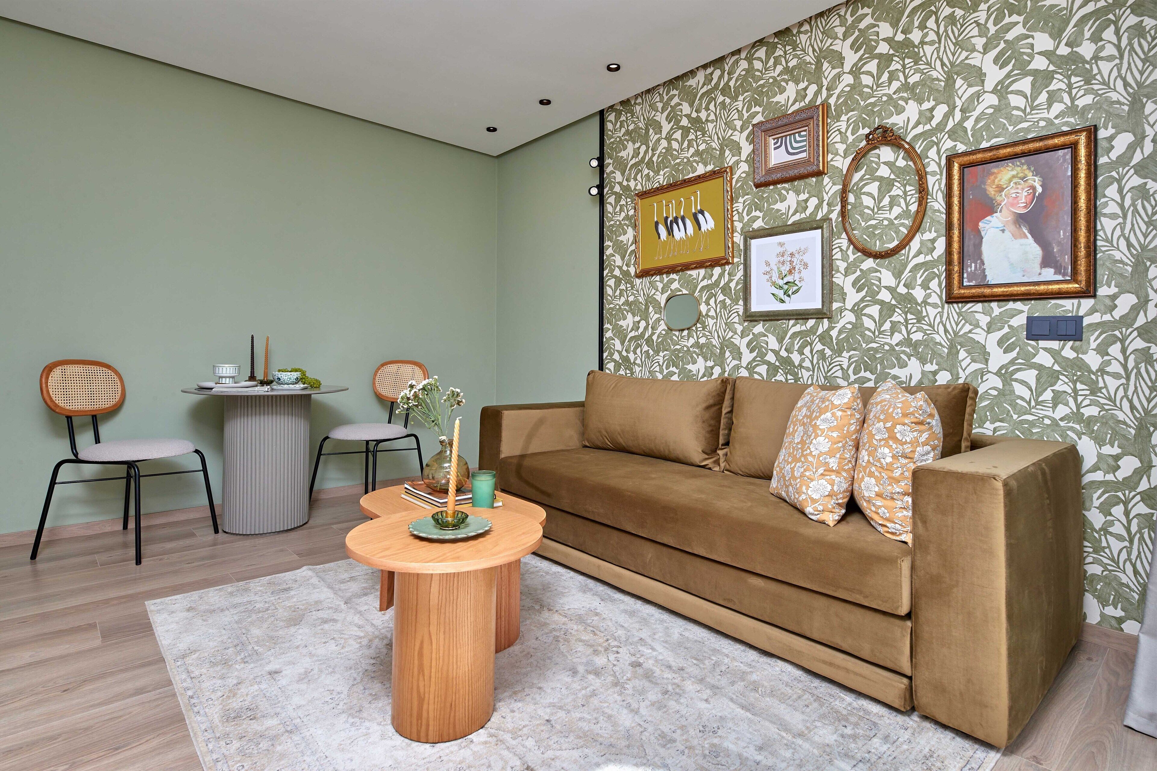 A living room with a brown sofa, two wicker chairs, a round wooden coffee table, and a patterned wallpaper.