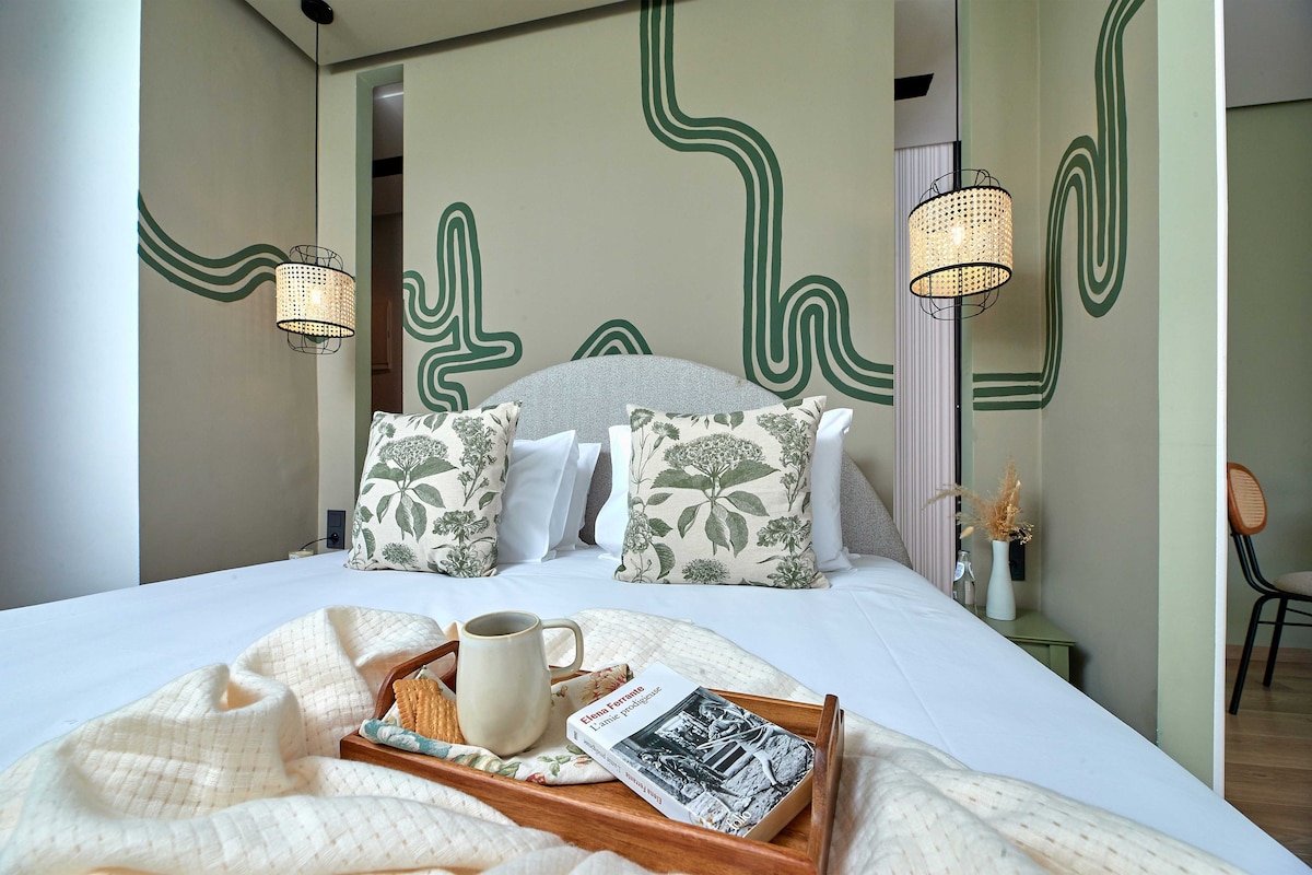 A neatly made bed with floral pillows, a tray with a mug and a book, and two wall-mounted lamps.