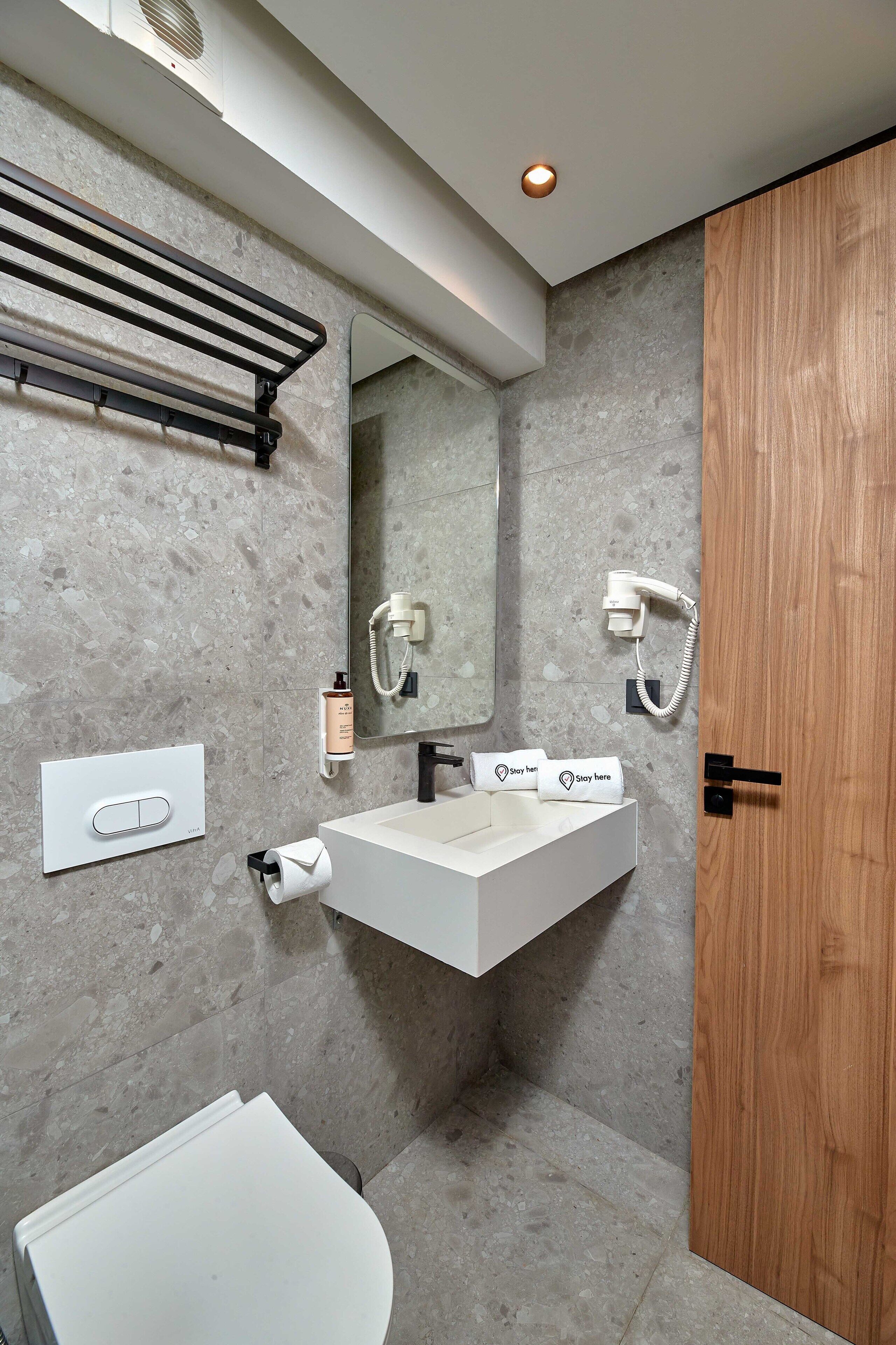 Een moderne badkamer met een witte wastafel, een handdoekdispenser, een spiegel en een houten deur.