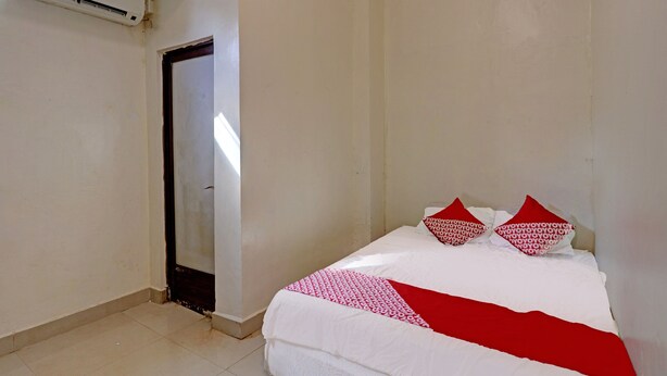 A small, sparsely furnished room with a bed, a door, and an air conditioning unit. - Hotel O Octav Homestay (Batam)