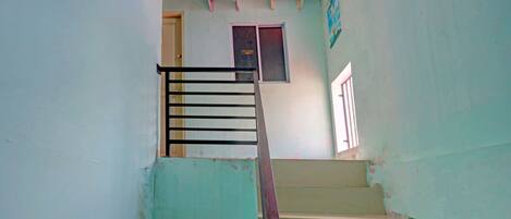 Una escalera con barandilla de metal que lleva a una plataforma con dos unidades de aire acondicionado y una puerta.