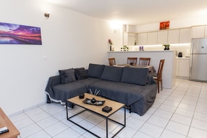 A compact living space with a sofa, a coffee table, a kitchen area with cabinets and a refrigerator, and a painting on the wall.