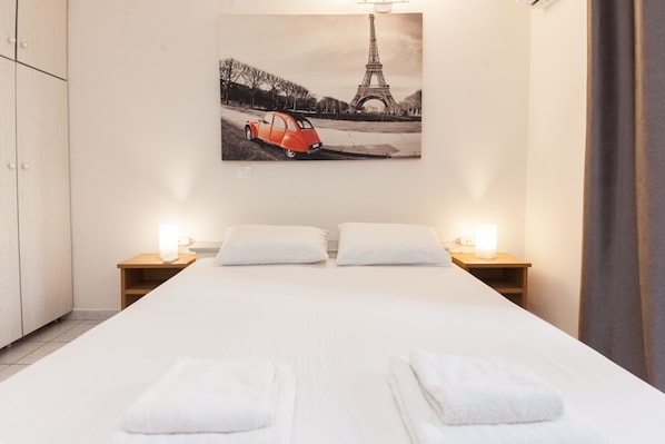 A hotel room with a bed, two bedside tables with lamps, a wall-mounted picture of the Eiffel Tower, and a curtain.