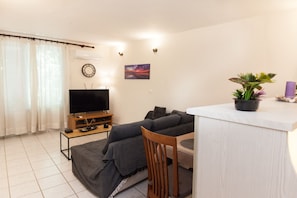 A living room with a sofa, a TV, a small table, a potted plant, and a painting on the wall.