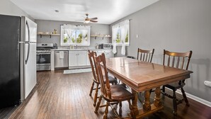 Une cuisine moderne avec une table et des chaises en bois, des appareils électroménagers en acier inoxydable et un ventilateur de plafond.