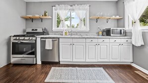 Une cuisine avec des meubles blancs, une cuisinière en acier inoxydable, un four à micro-ondes et une fenêtre avec des rideaux.