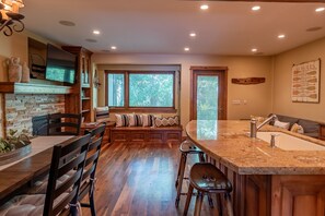 A modern kitchen with a stone fireplace, wooden cabinetry, and a large island with a sink.