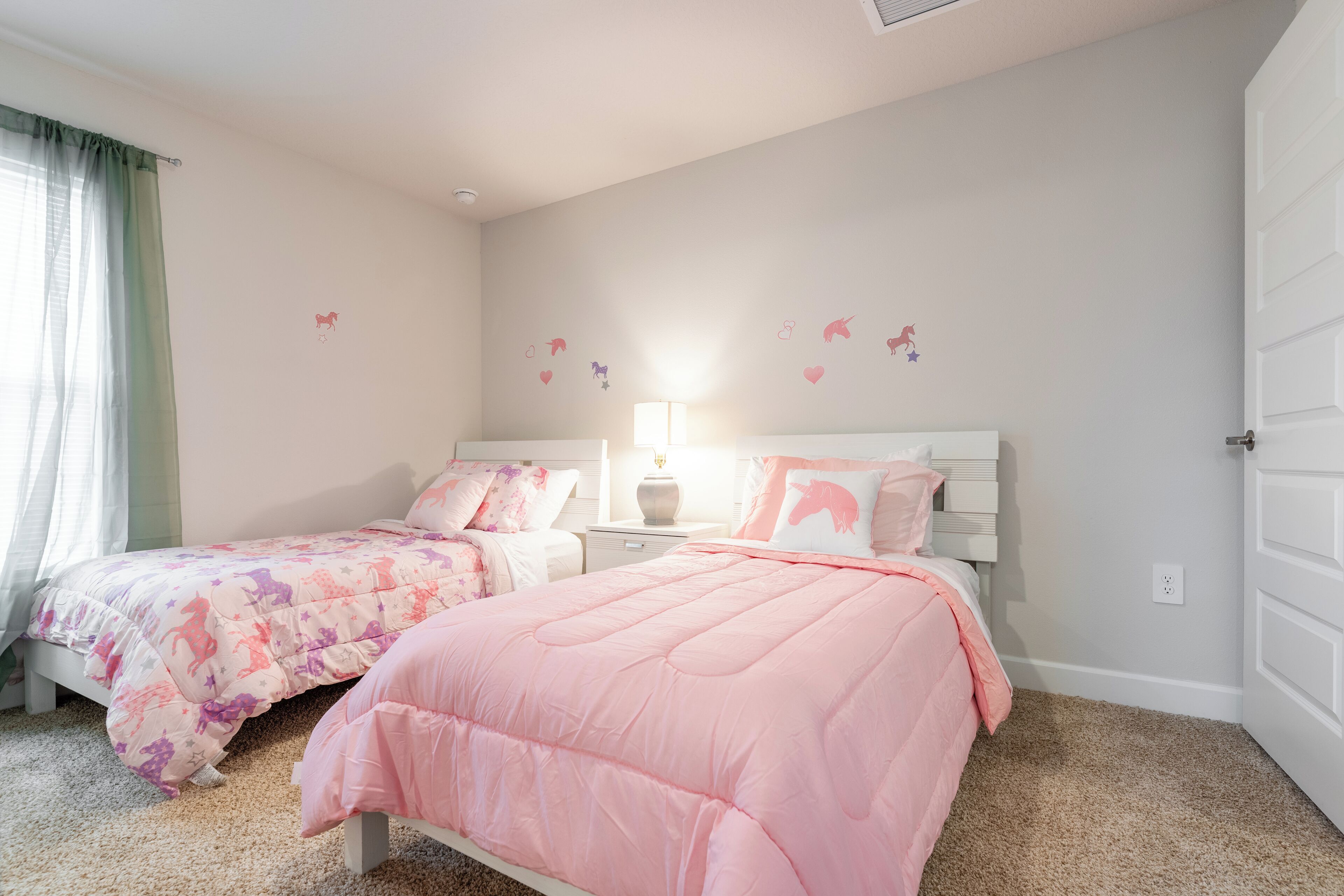 A bedroom with two beds, a nightstand, a lamp, and a door.