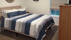 Une chambre à coucher avec un lit, un miroir rond, un élément de décoration sur le thème de l’ancre, une télévision et une fenêtre avec des stores.