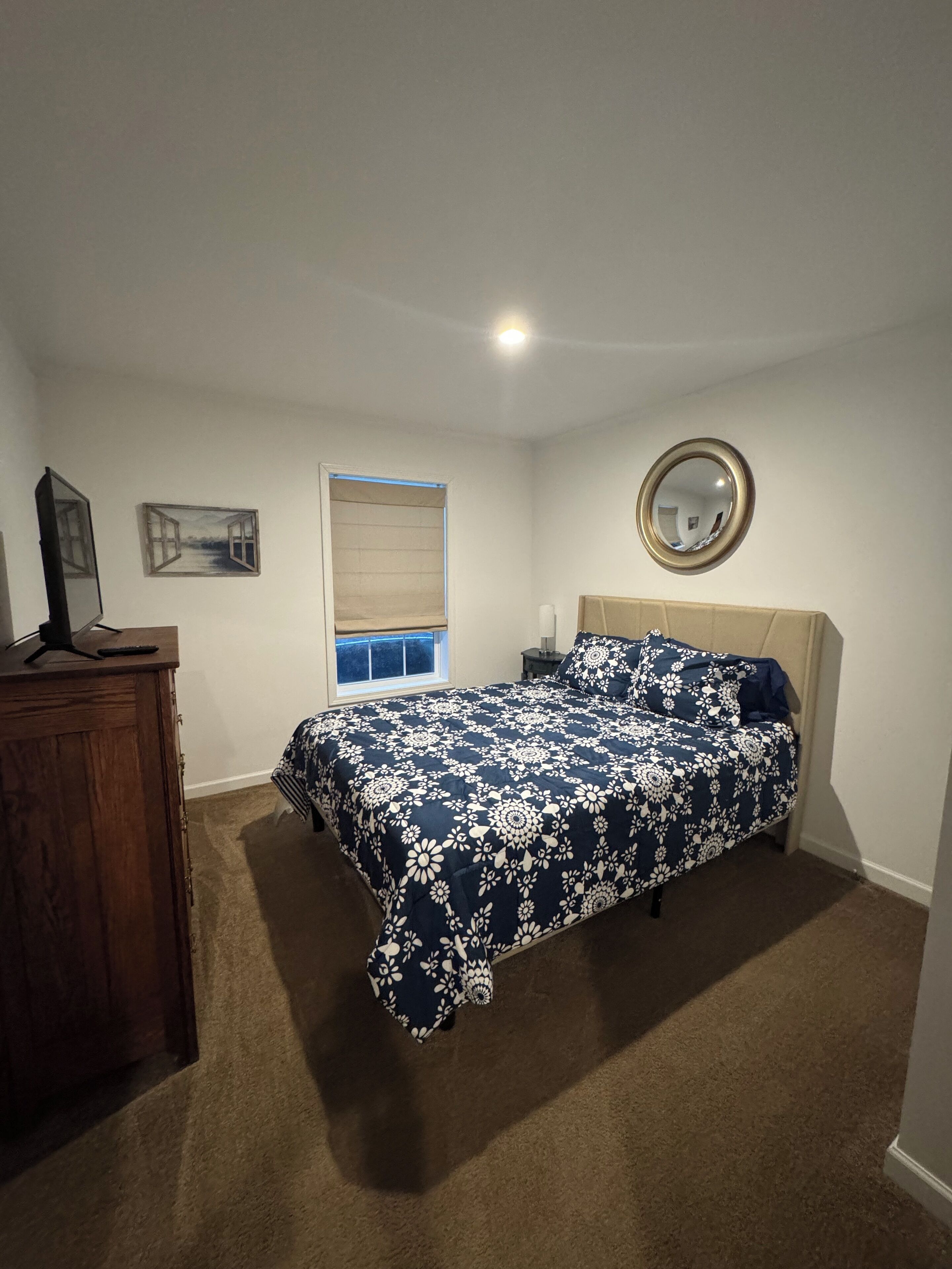 Une chambre à coucher avec un lit, une commode, une fenêtre donnant sur un beau paysage, un miroir et un tableau au mur.