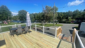 Une terrasse en bois avec des meubles d’extérieur, une vue sur un lac et un drapeau.