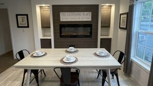 Un coin repas avec une longue table dressée pour quatre personnes, une cheminée et une pancarte indiquant : « Le lieu de rencontre ».