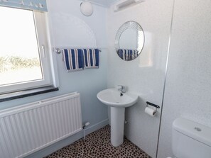 A bathroom with a white sink, a round mirror, and striped towels hanging on a rack.