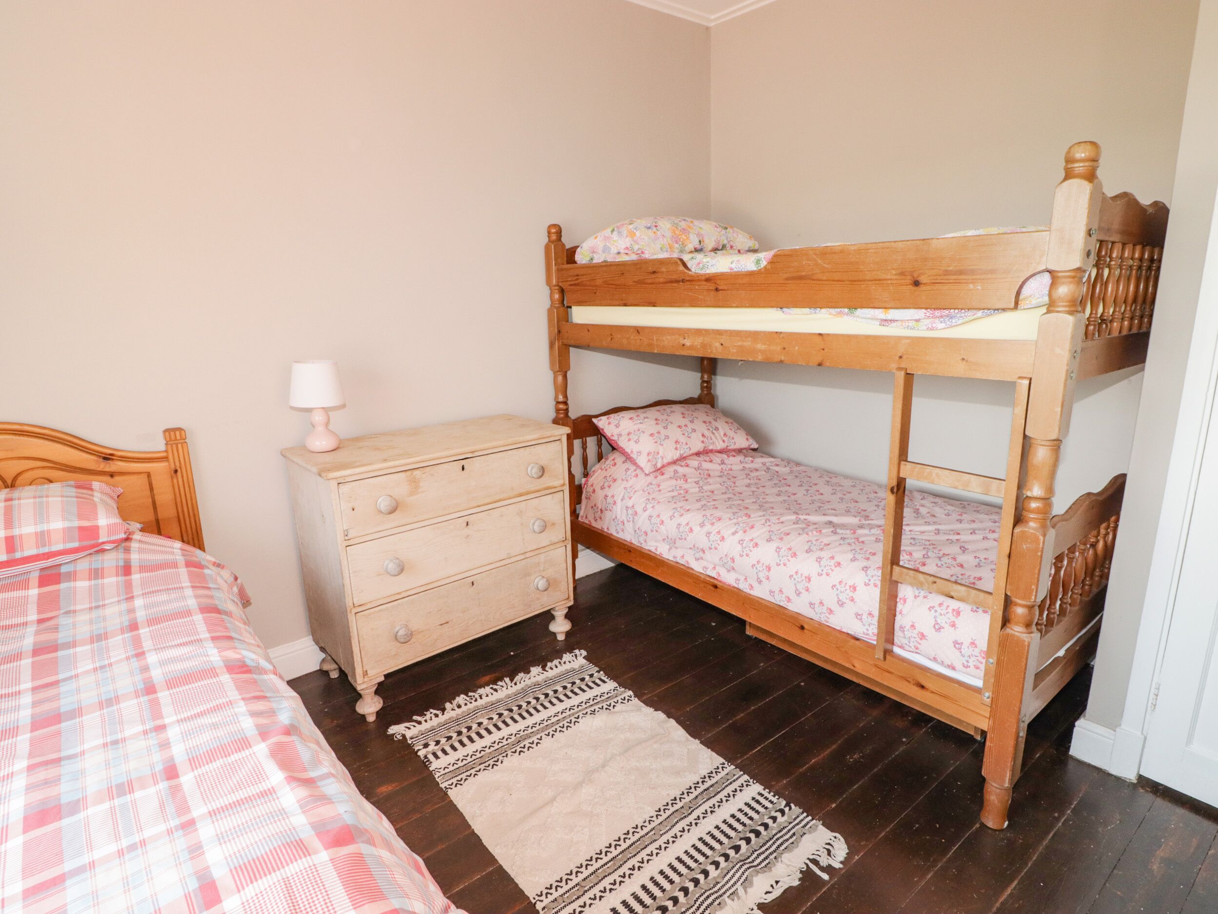 A bunk bed with a wooden headboard, a dresser with drawers, a lamp, and a patterned rug on a wooden floor.