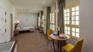 Una habitación de hotel con cama, una mesita con sillas, ventana con cortinas y suelo de madera.
