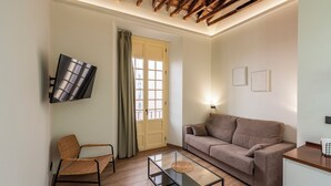 Una sala de estar con sofá, sillón, mesa de centro, televisor y una puerta con cortinas.