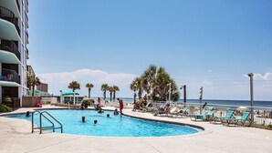 A swimming pool area with lounge chairs and palm trees, adjacent to a building with balconies. - Watercrest #807 | Beach Views + Resort Pool! (Panama City Beach)