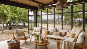 Ein gemütlicher, offener Wohnbereich mit großem Fenster und Blick auf einen Garten, ausgestattet mit einer Couch, Sesseln und einem Couchtisch.