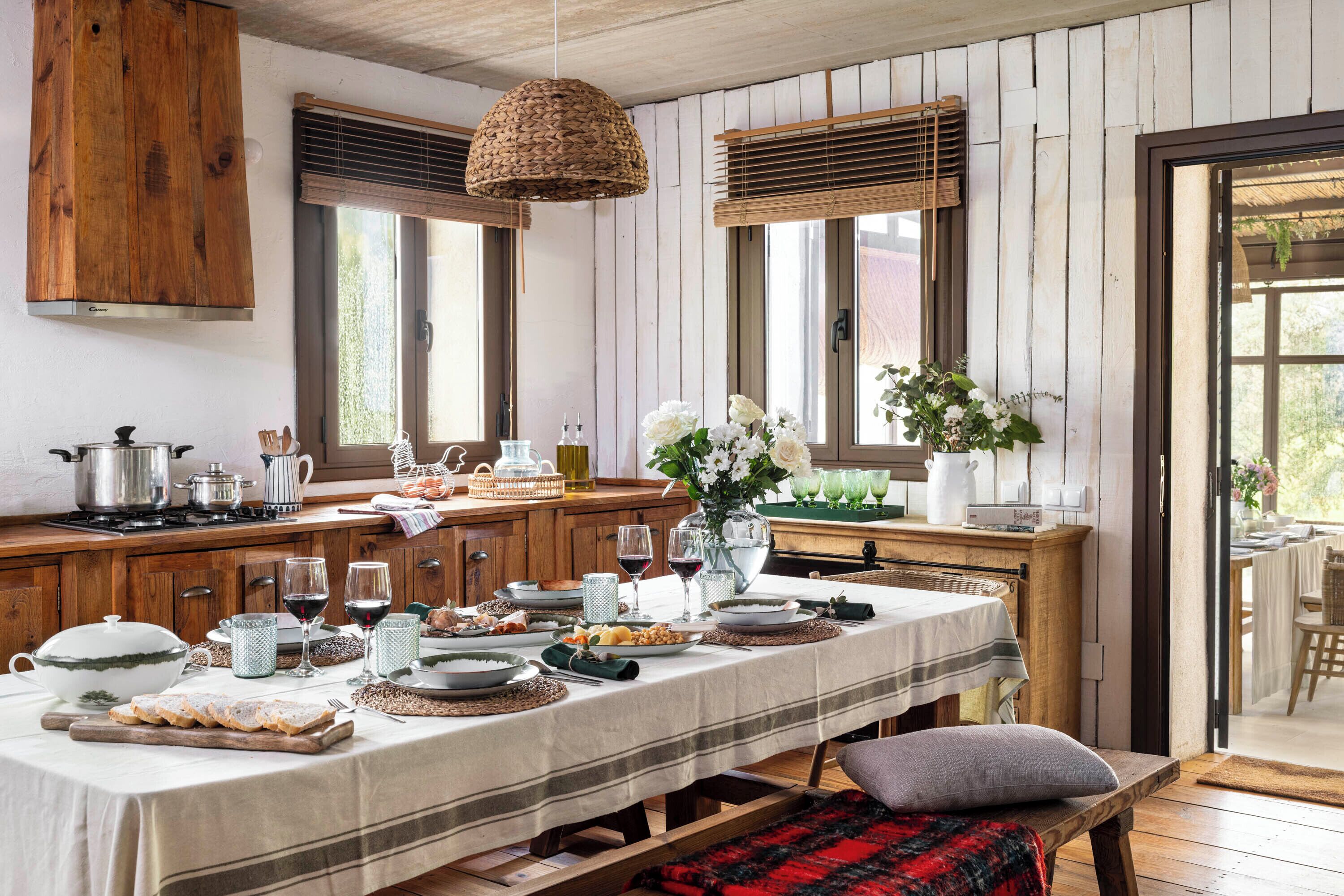 Una cocina rústica con armarios de madera, una mesa de comedor dispuesta para una comida y un banco con una manta.