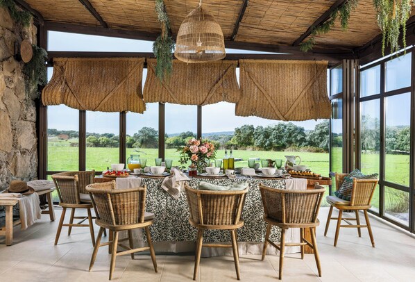 A dining area with wicker chairs and a table set for six, overlooking a green landscape.