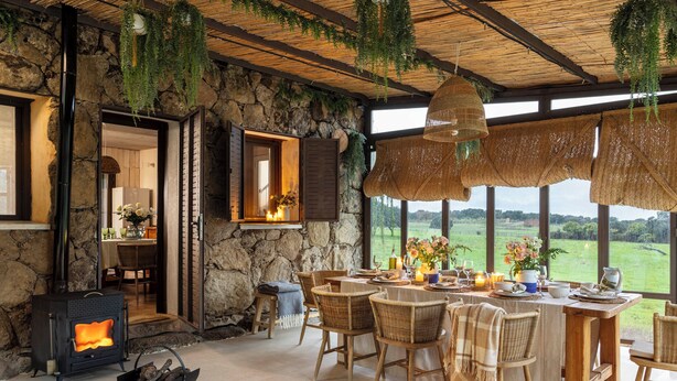 Ein rustikaler Essbereich mit Steinwänden, einem Kamin, Korbmöbeln und Blick auf die Landschaft.