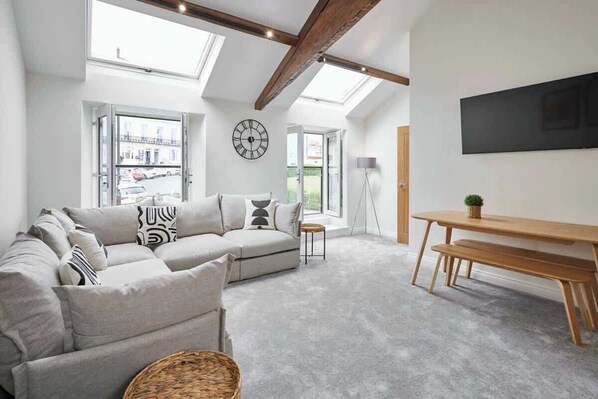 A modern living room with a sectional sofa, a wooden bench, a round table, and a large wall clock.