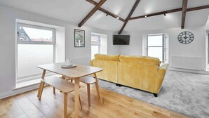 A modern living room with a wooden table, yellow sofa, and large windows. - Host & Stay | 3 The Mount (Whitby)
