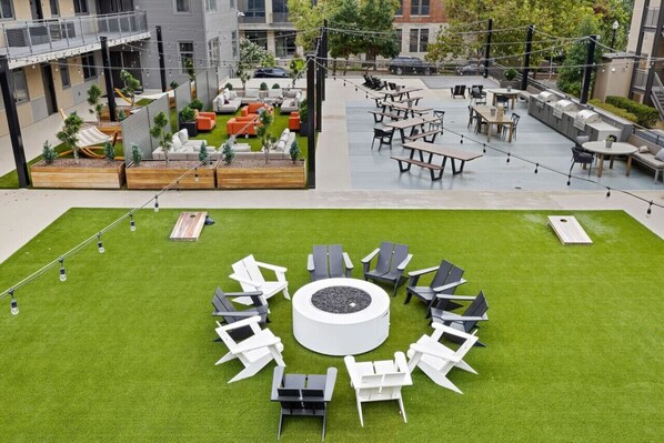 Un espacio patio al aire libre con arreglos de asientos, un brasero central y vistas de los edificios circundantes.