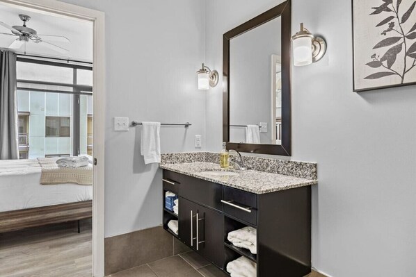 Un baño moderno con encimera de granito, un espejo grande y un ventilador de techo.