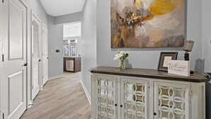 Un pasillo con piso de madera clara, puertas blancas y un aparador decorativo con un cartel que dice 'Welcome Home'.