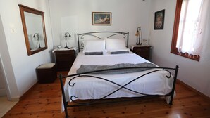 Een slaapkamer met een bed, houten vloeren, een grote spiegel, nachtkastjes en kunstwerken aan de muren.