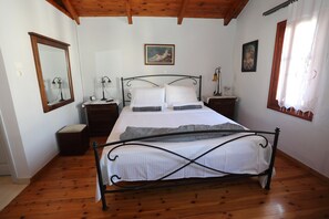 A bedroom with a bed, wooden floors, a large mirror, bedside tables, and artwork on the walls.