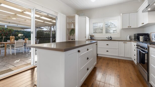 A modern kitchen with white cabinetry, a central island, and a dining area with outdoor seating. - Sampson Cottage | Historic Charm (Orange)