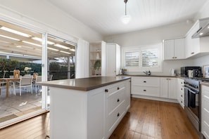 A modern kitchen with white cabinetry, a central island, and a dining area with outdoor seating. - Sampson Cottage | Historic Charm (Orange)