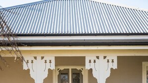 A house with a corrugated metal roof, a white picket fence, and a number '14' sign. - Sampson Cottage | Historic Charm (Orange)