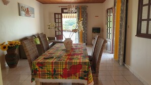 Un coin repas avec une table recouverte d’une nappe à motifs floraux, des chaises en osier et un vase rempli de tournesols.