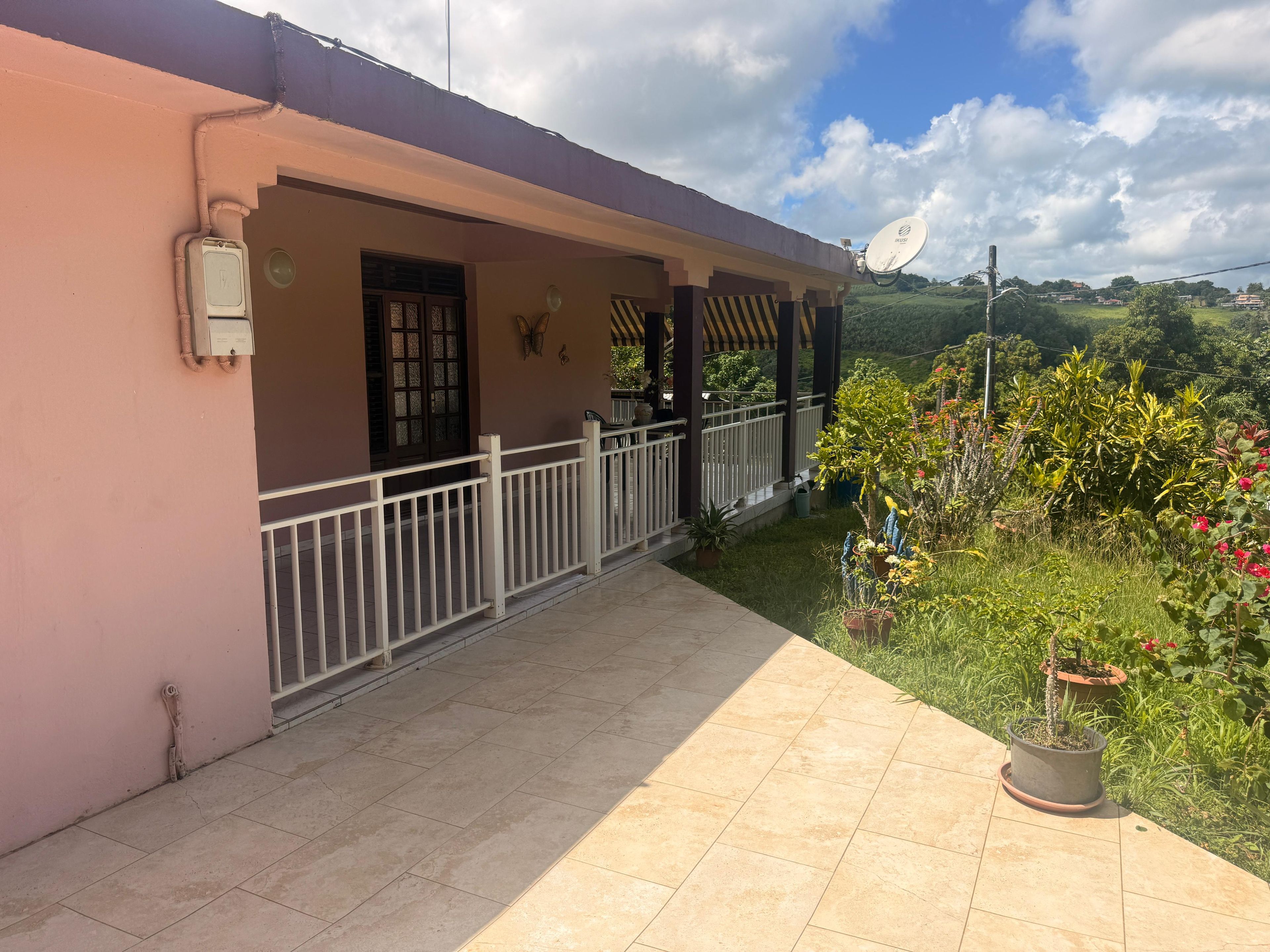 A building with a covered porch, a satellite dish, and a garden with potted plants.