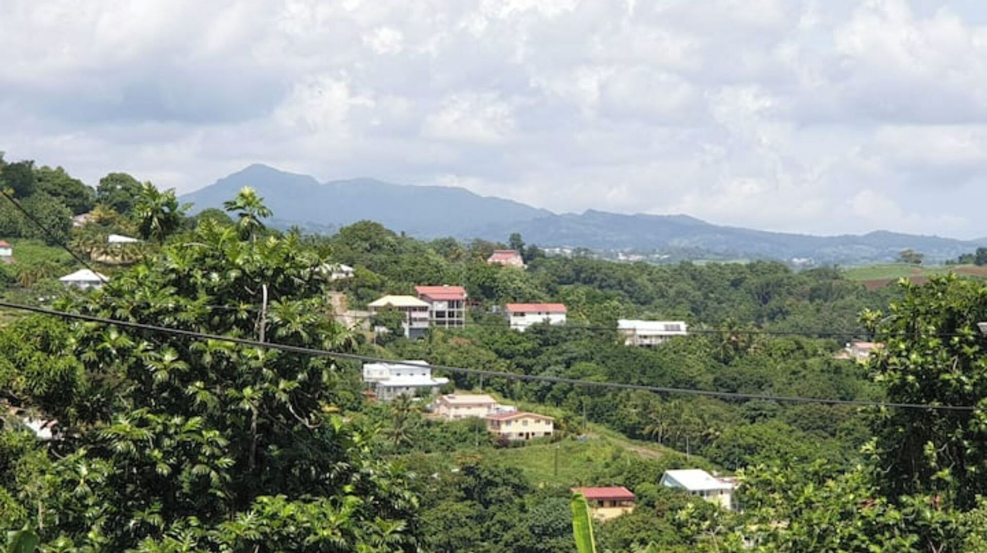Un village perché sur une colline, avec ses maisons et sa végétation luxuriante, entouré de montagnes.
