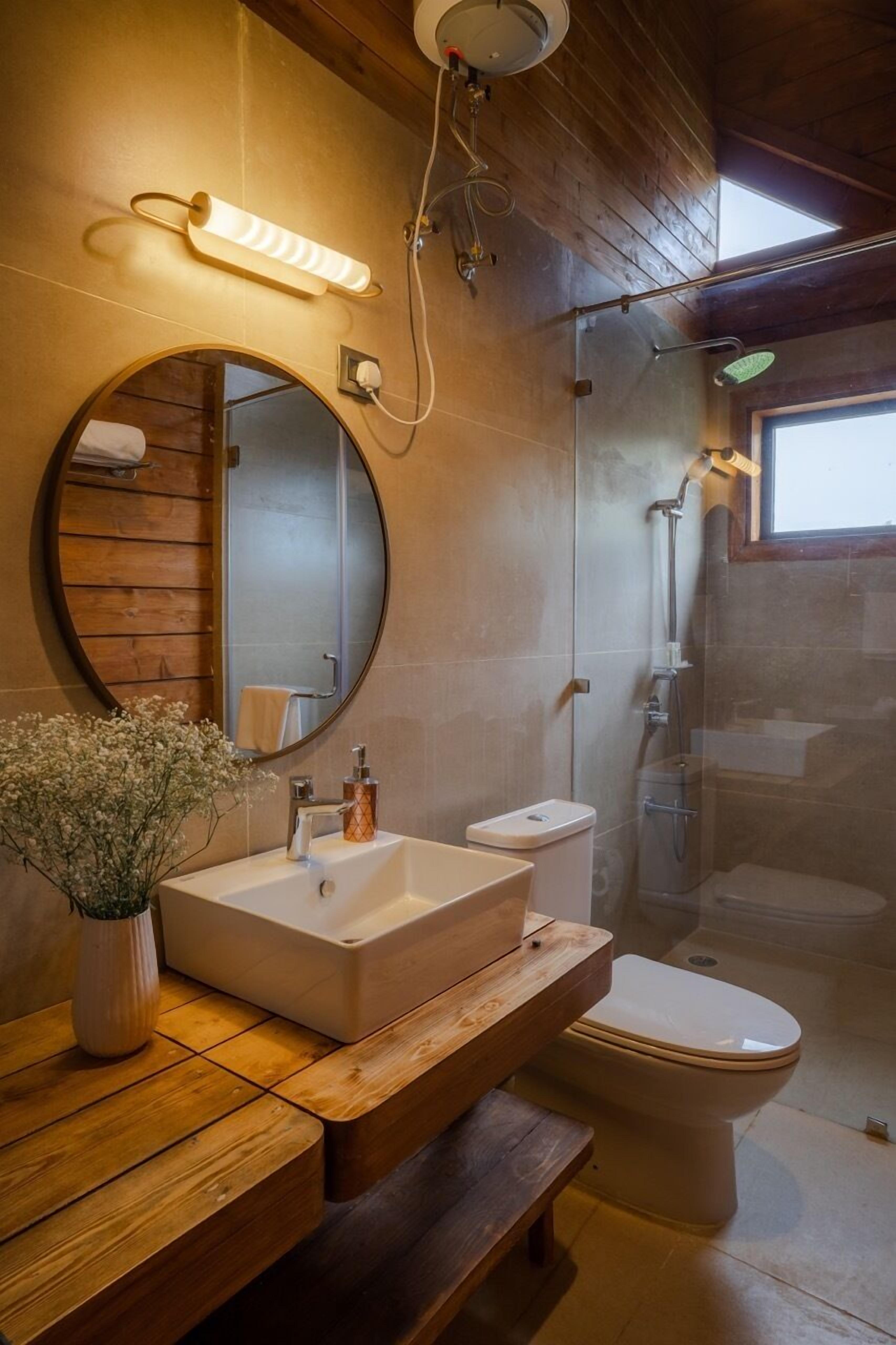 Une salle de bain moderne avec un meuble-lavabo en bois, un miroir rond, des toilettes et une douche à parois de verre.